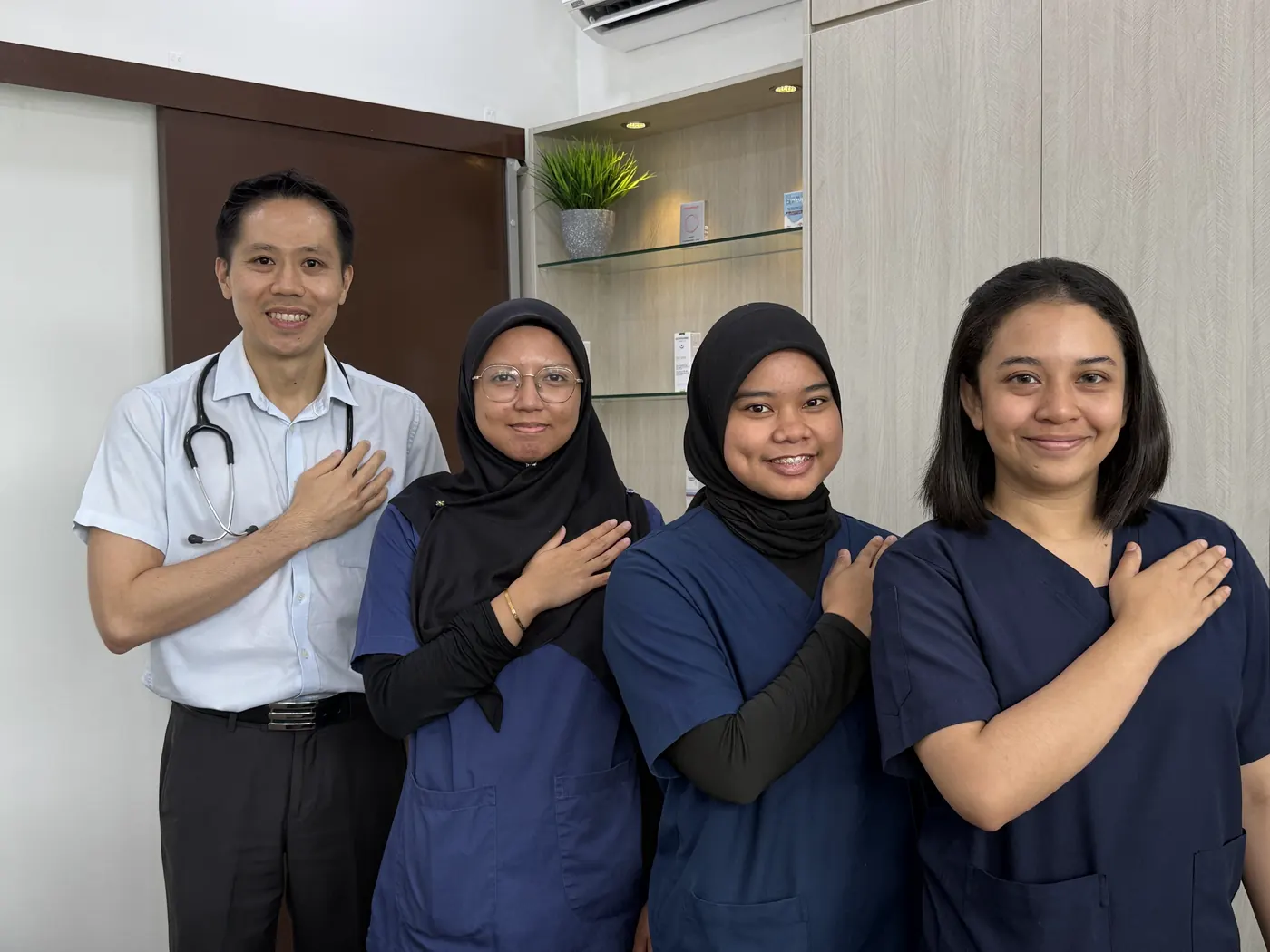 Four Klinik Astracare team members standing in a row with their hands over their hearts inside the clinic